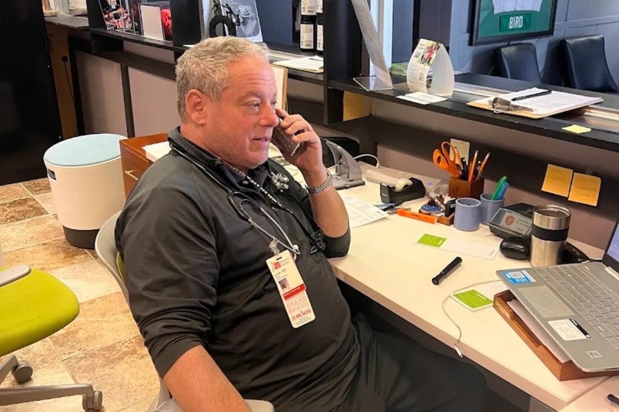 Dr. Leve taking a call at the front desk of the clinic on South High Street, stethoscope around his neck and badge clipped to his shirt.