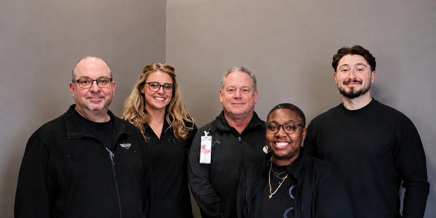 The five people who staff German Village Men's Clinic, standing together in black GVMC layers against a grey studio wall.